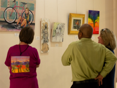 Three people gather around art that is hung on the wall.