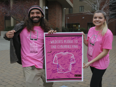 A women and man stand next to each other in pink shirts holding a sign. The sign says 